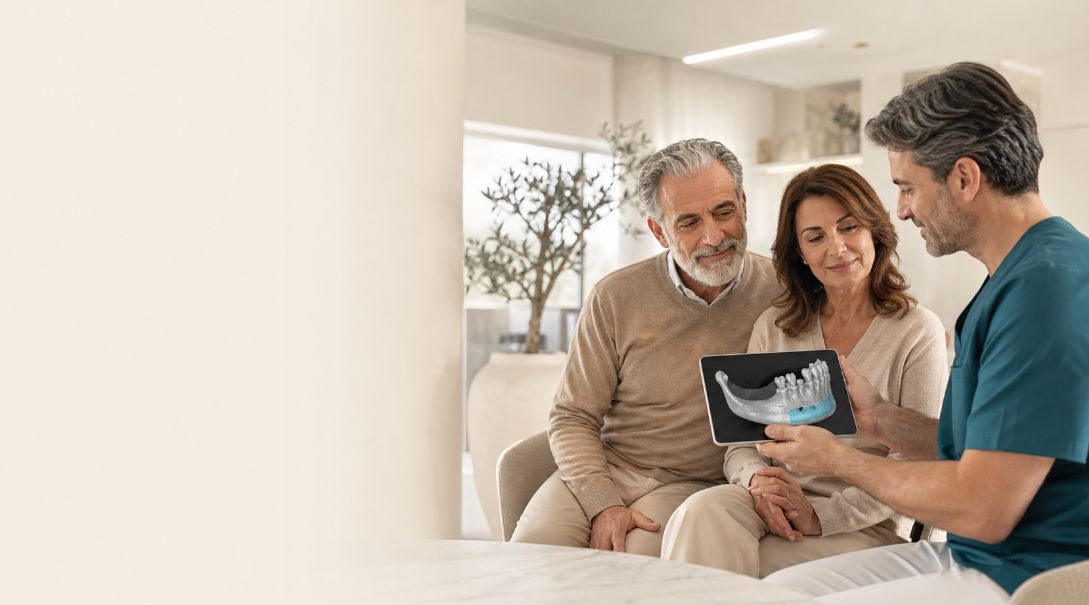 Coppia italiana anziana in una consulenza implantare con dentista che esamina una scansione 3D per pianificare un innesto osseo dentale prima degli impianti.